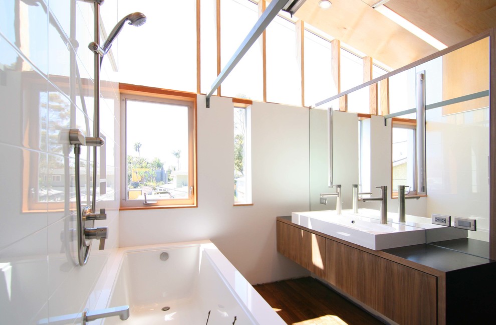 Modernes Badezimmer mit Aufsatzwaschbecken, flächenbündigen Schrankfronten, dunklen Holzschränken, Waschtisch aus Holz, Badewanne in Nische, Duschbadewanne und weißen Fliesen in Los Angeles