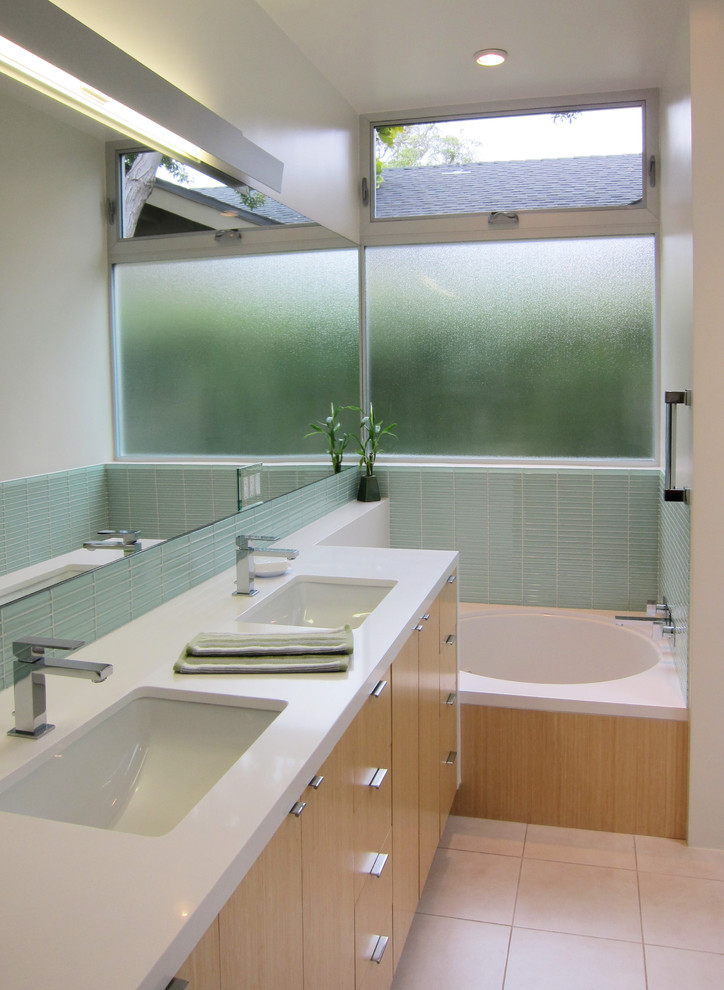 Exemple d'une salle de bain moderne en bois clair avec un lavabo encastré, un placard à porte plane, un carrelage bleu, un carrelage en pâte de verre, une baignoire en alcôve et un plan de toilette blanc.