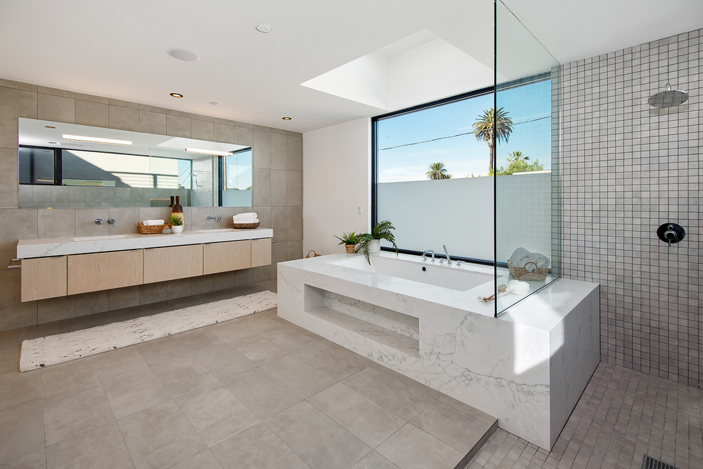 На фото: ванная комната в современном стиле с плоскими фасадами, светлыми деревянными фасадами, полновстраиваемой ванной, серой плиткой, белыми стенами, врезной раковиной, серым полом и белой столешницей