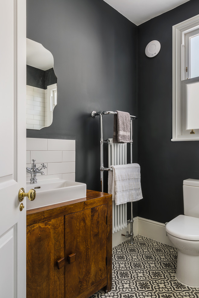 Klassisk inredning av ett litet badrum, med släta luckor, skåp i mörkt trä, en toalettstol med hel cisternkåpa, grå väggar, klinkergolv i keramik och ett fristående handfat
