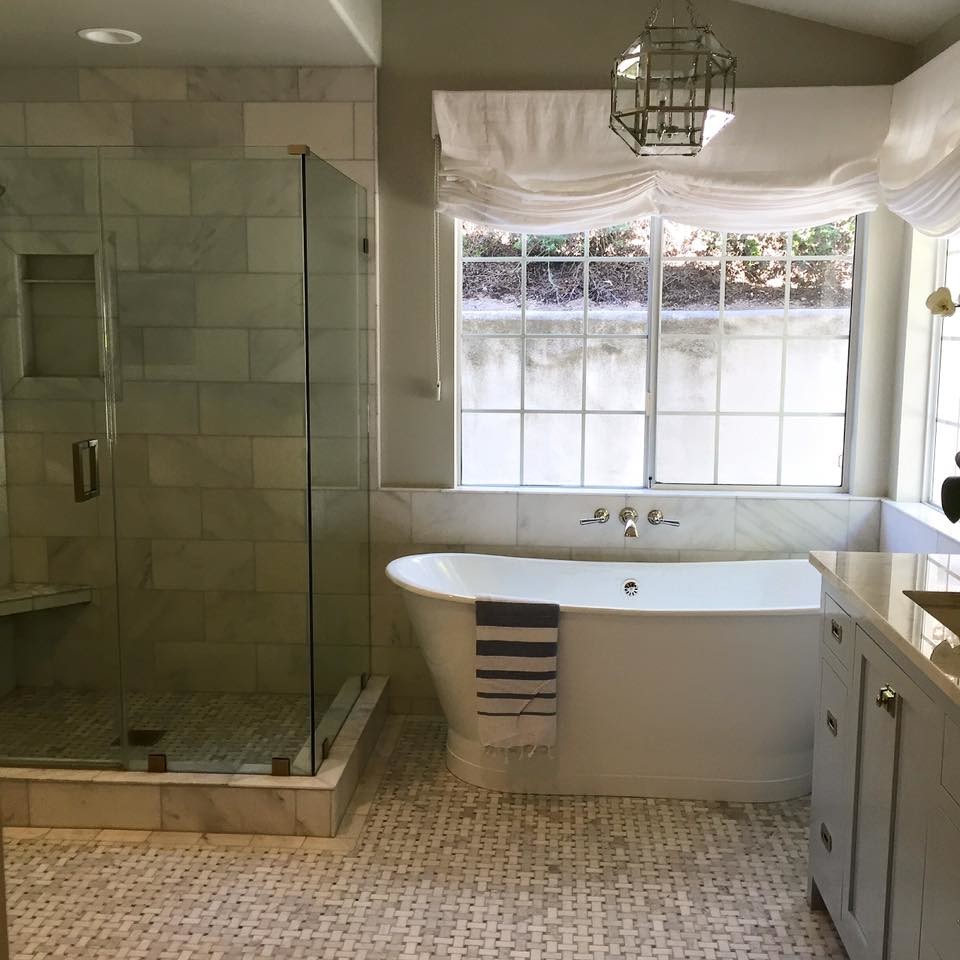 Cette photo montre une grande salle de bain principale bord de mer avec des portes de placard bleues, une baignoire indépendante, une douche d'angle, WC à poser, un carrelage gris, un carrelage de pierre, un mur gris, un sol en marbre, un lavabo encastré et un plan de toilette en marbre.