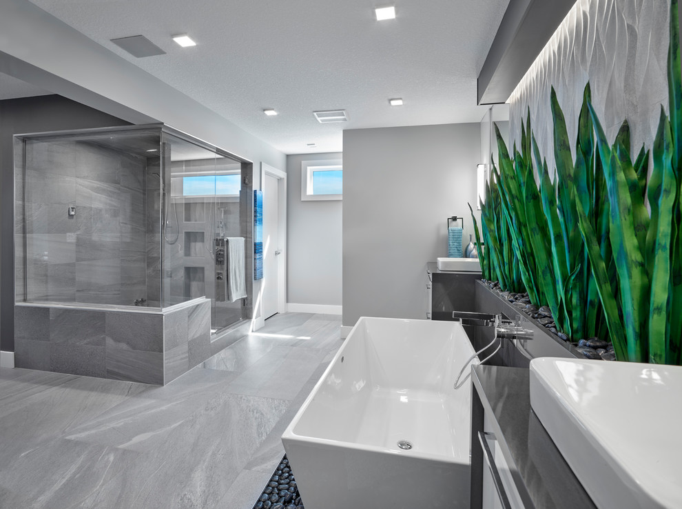 Photo of a large contemporary ensuite bathroom in Edmonton with grey cabinets, a freestanding bath, grey tiles, ceramic tiles, grey walls, ceramic flooring, grey floors, grey worktops and engineered stone worktops.