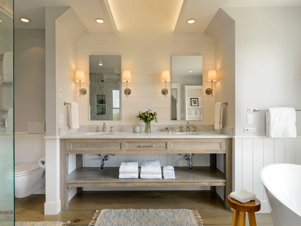 Lantlig inredning av ett grå grått en-suite badrum, med grå skåp, ett fristående badkar, en hörndusch, en vägghängd toalettstol, grå väggar, mellanmörkt trägolv, ett undermonterad handfat, grått golv och luckor med infälld panel