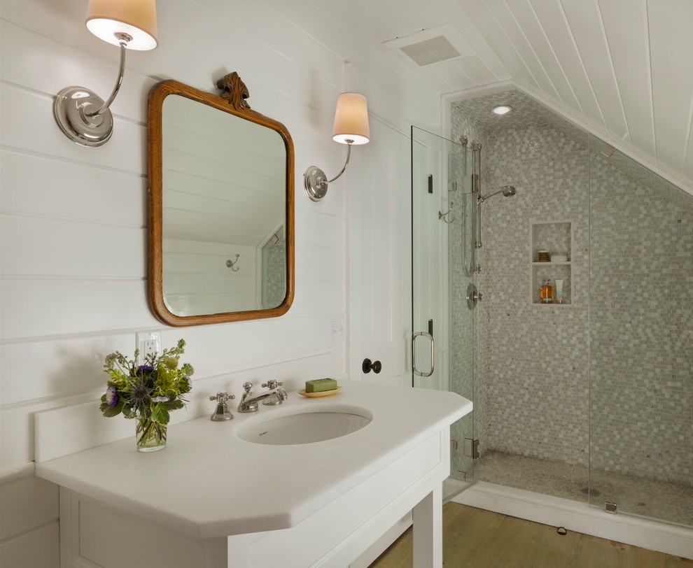 Farmhouse shower room bathroom in Burlington with white cabinets, an alcove shower, grey tiles, white tiles, mosaic tiles, white walls, medium hardwood flooring, a submerged sink, brown floors and a hinged door.