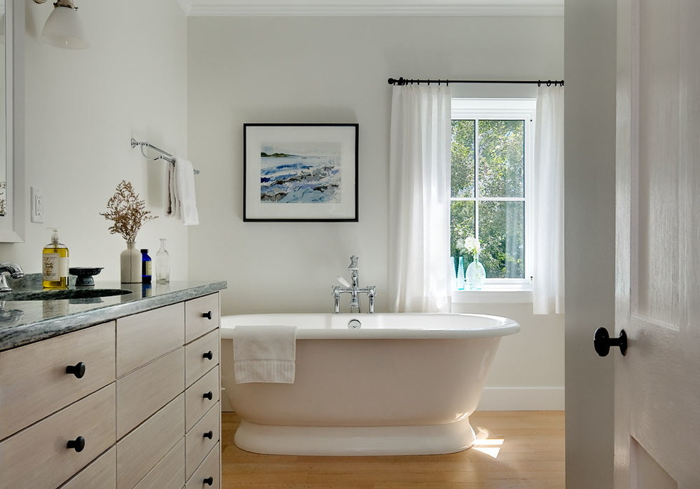 Bild på ett mellanstort vintage en-suite badrum, med släta luckor, skåp i ljust trä, ett fristående badkar, vita väggar, ljust trägolv, ett undermonterad handfat och granitbänkskiva