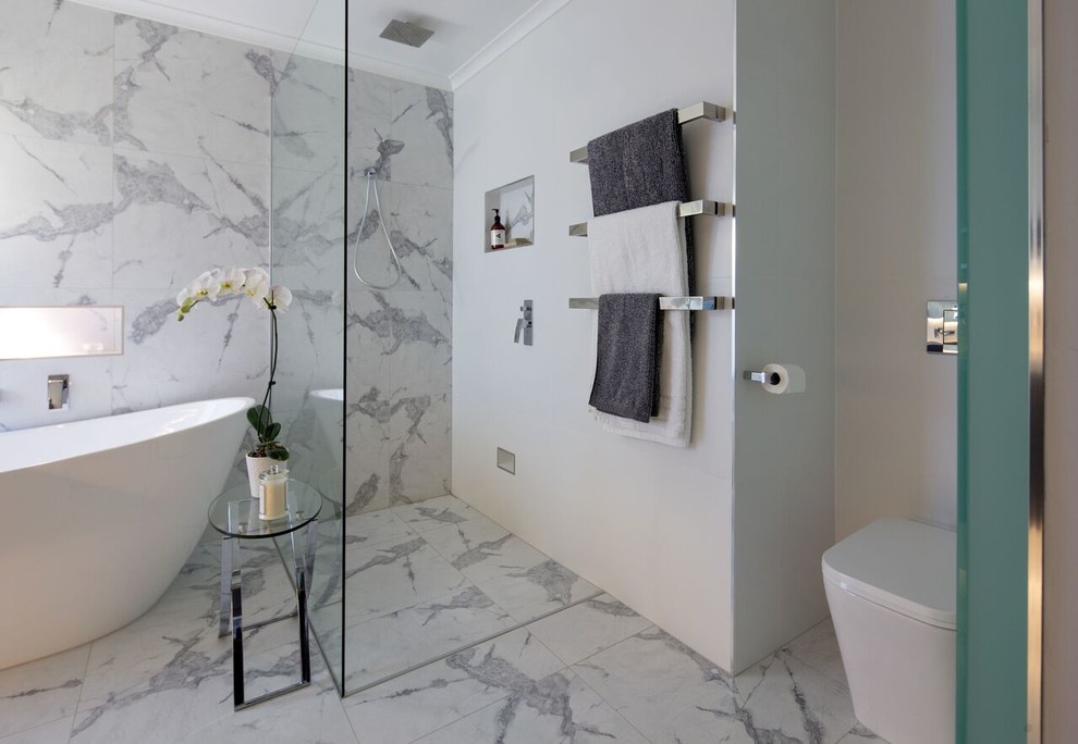 Свежая идея для дизайна: главная ванная комната среднего размера в стиле модернизм с отдельно стоящей ванной, душем без бортиков, инсталляцией, белой плиткой, керамогранитной плиткой, белыми стенами и полом из керамогранита - отличное фото интерьера