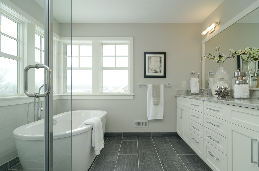 Lantlig inredning av ett badrum, med skåp i shakerstil, vita skåp, ett fristående badkar och grå kakel
