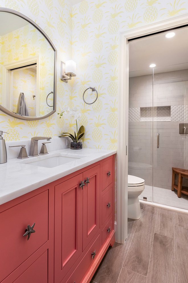 Cette photo montre une salle de bain bord de mer avec un placard avec porte à panneau encastré, des portes de placard rouges, un mur jaune, un lavabo encastré, un sol gris, une cabine de douche à porte battante et un plan de toilette blanc.