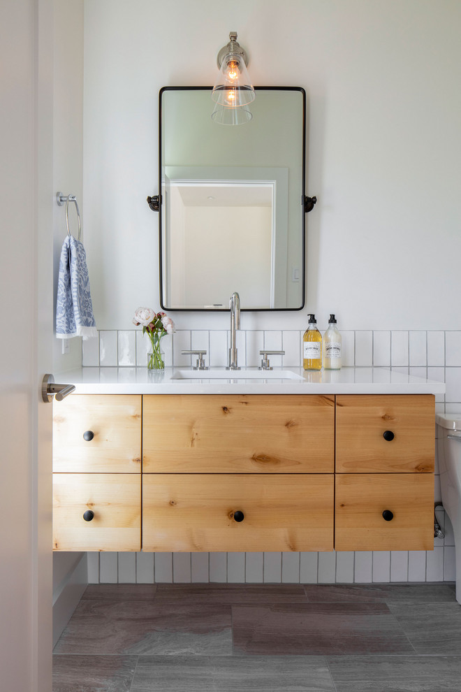 Idée de décoration pour une salle de bain champêtre en bois clair avec un placard à porte plane, un carrelage blanc, un mur blanc, un lavabo encastré, un sol gris et un plan de toilette blanc.