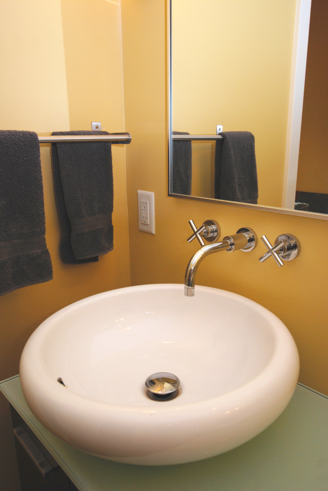 Foto på ett stort funkis badrum, med ett fristående handfat, beige skåp, bänkskiva i glas, ett badkar med tassar och gula väggar