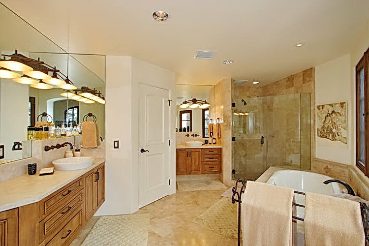 This is an example of a large mediterranean ensuite bathroom in San Diego with beaded cabinets, medium wood cabinets, a built-in bath, a corner shower, a one-piece toilet, beige tiles, travertine tiles, white walls, travertine flooring, a vessel sink, granite worktops, beige floors and a hinged door.