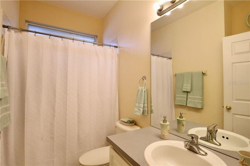 Photo of a medium sized traditional family bathroom in Orlando with raised-panel cabinets, white cabinets, an alcove bath, a shower/bath combination, a one-piece toilet, beige tiles, ceramic tiles, white walls, ceramic flooring, a built-in sink, laminate worktops, beige floors, a shower curtain, grey worktops, double sinks and a built in vanity unit.