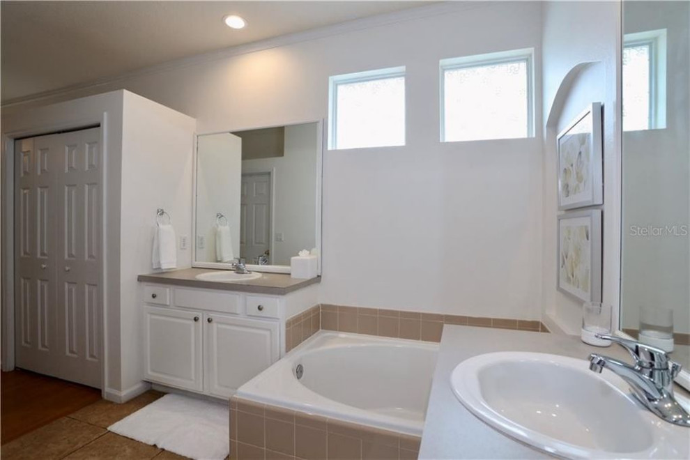 Medium sized traditional ensuite bathroom in Orlando with raised-panel cabinets, white cabinets, a built-in bath, a corner shower, a one-piece toilet, beige tiles, ceramic tiles, white walls, ceramic flooring, a built-in sink, laminate worktops, beige floors, a sliding door, grey worktops, double sinks and a built in vanity unit.