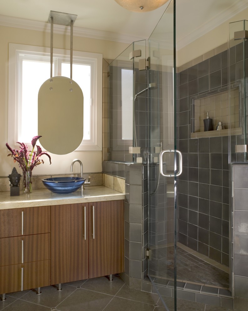 Modern inredning av ett mellanstort badrum med dusch, med ett fristående handfat, släta luckor, en hörndusch, beige väggar, skåp i mellenmörkt trä, bänkskiva i kalksten, en toalettstol med separat cisternkåpa, grå kakel, keramikplattor och kalkstensgolv