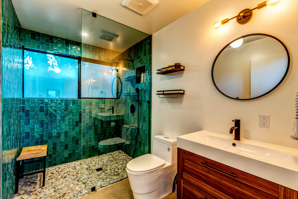 Foto på ett litet funkis badrum med dusch, med släta luckor, skåp i mellenmörkt trä, en kantlös dusch, en toalettstol med hel cisternkåpa, grön kakel, glaskakel, vita väggar, betonggolv, ett avlångt handfat, grått golv och med dusch som är öppen