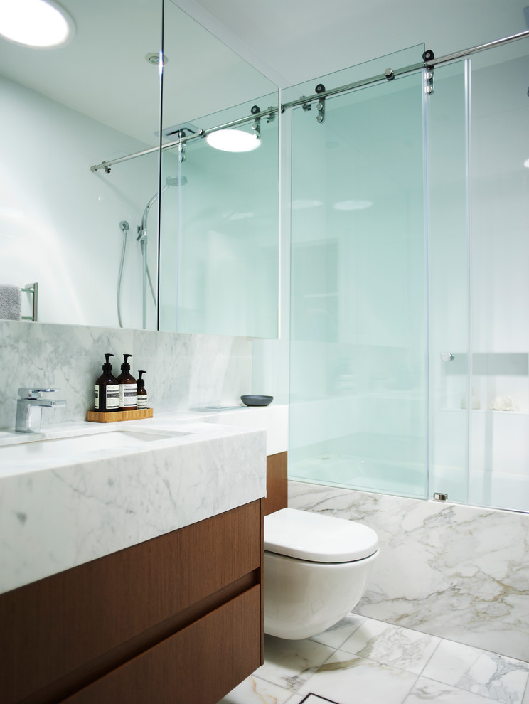 Design ideas for a contemporary bathroom in Sydney with medium wood cabinets, a built-in bath, a shower/bath combination, a wall mounted toilet, marble tiles, marble flooring, marble worktops and a hinged door.