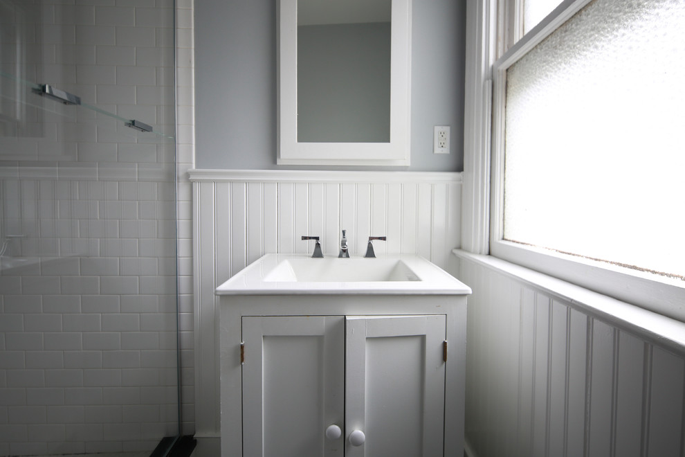 Klassisk inredning av ett mellanstort vit vitt badrum med dusch, med vita skåp, en hörndusch, en toalettstol med separat cisternkåpa, vit kakel, keramikplattor, grå väggar, klinkergolv i keramik, ett integrerad handfat, flerfärgat golv och dusch med gångjärnsdörr