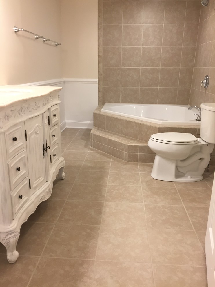 Klassisk inredning av ett stort en-suite badrum, med möbel-liknande, vita skåp, ett platsbyggt badkar, en dusch/badkar-kombination, en toalettstol med hel cisternkåpa, beige kakel, porslinskakel, beige väggar, klinkergolv i porslin, ett undermonterad handfat, marmorbänkskiva, beiget golv och dusch med duschdraperi