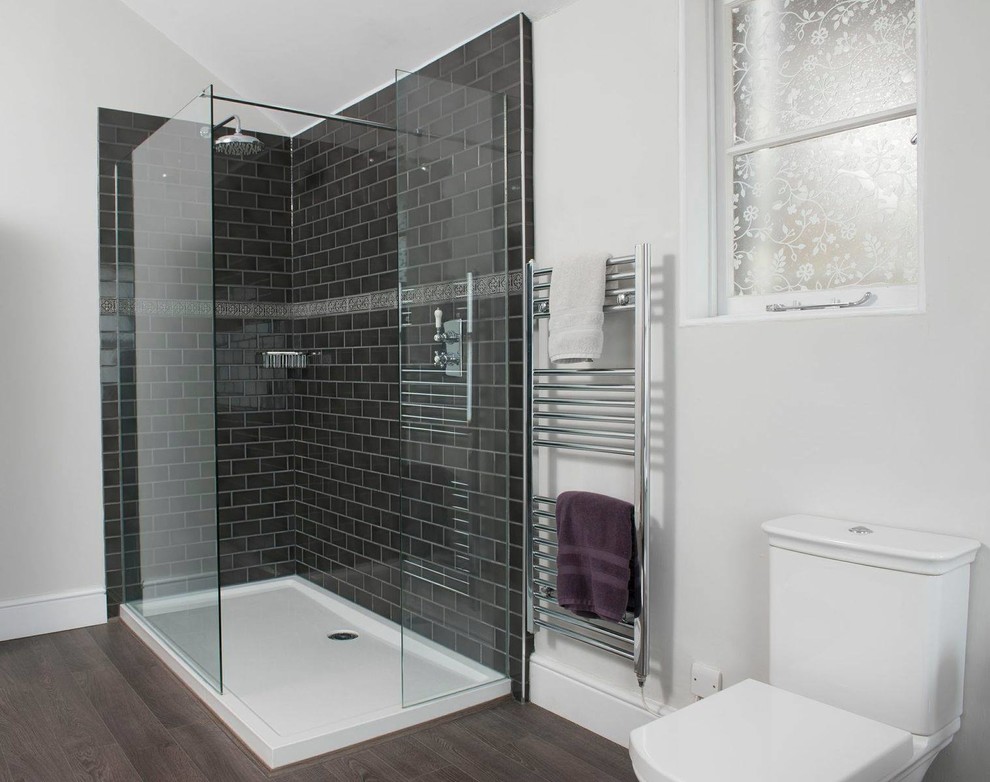 Diseño de cuarto de baño moderno de tamaño medio con ducha esquinera, sanitario de una pieza, baldosas y/o azulejos negros, baldosas y/o azulejos de cerámica, paredes grises y suelo de madera oscura