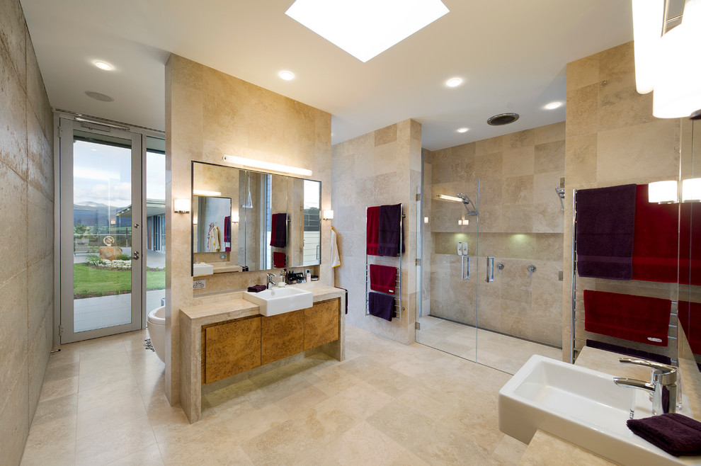 Cette image montre une grande salle de bain principale design en bois brun avec une baignoire indépendante, une douche double, WC à poser, un placard à porte plane, un carrelage beige, du carrelage en travertin, un mur beige, un sol en travertin, une grande vasque et un plan de toilette en calcaire.