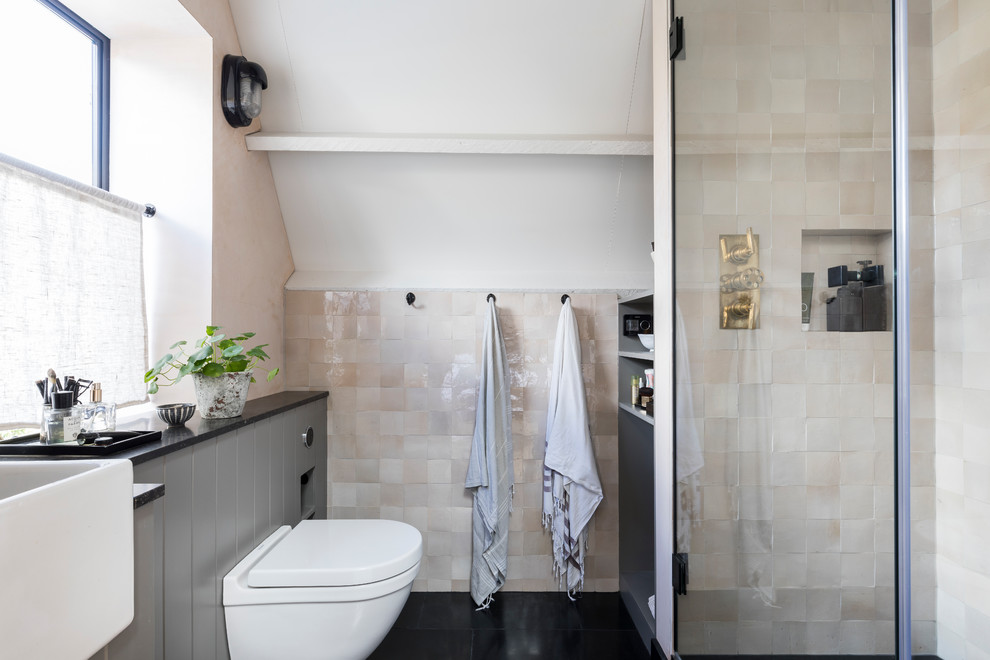 Urban ensuite bathroom in London with grey cabinets, a built-in shower, a wall mounted toilet, pink tiles, pink walls, limestone flooring, limestone worktops, black floors, a hinged door and black worktops.