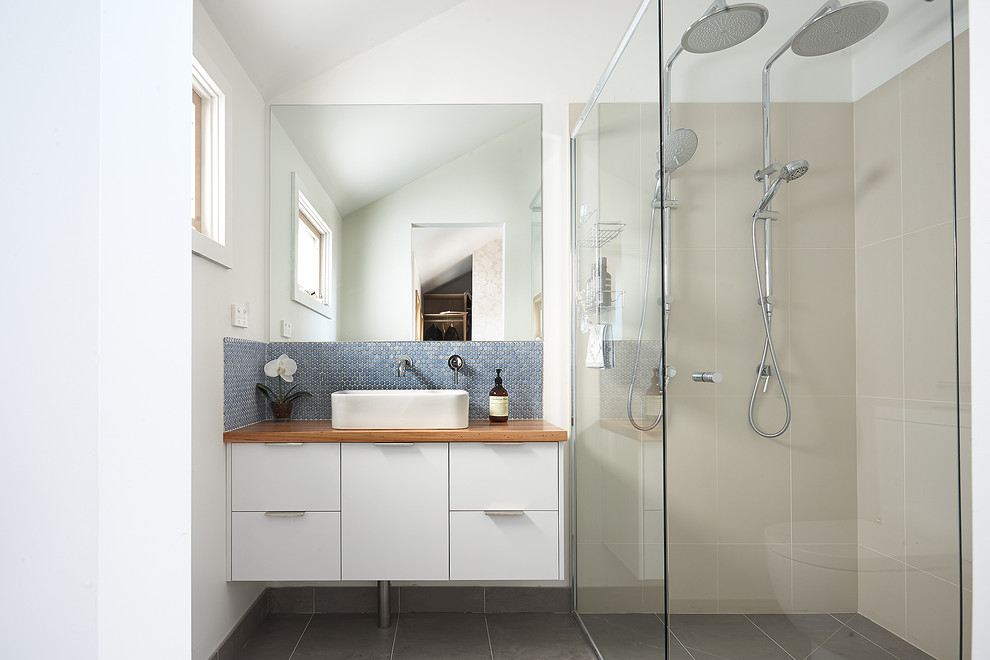 Пример оригинального дизайна: маленькая главная ванная комната в современном стиле с настольной раковиной, белыми фасадами, столешницей из дерева, двойным душем, синей плиткой, белыми стенами, унитазом-моноблоком, керамической плиткой, полом из керамогранита, коричневой столешницей, фасадами с выступающей филенкой, серым полом, душем с распашными дверями и окном для на участке и в саду