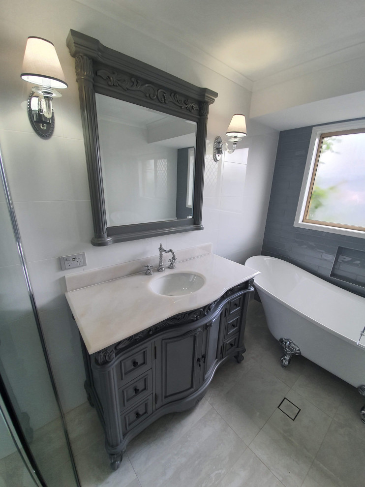 На фото: ванная комната среднего размера в викторианском стиле с серыми фасадами, ванной на ножках, угловым душем, белой плиткой, керамогранитной плиткой, полом из керамогранита, накладной раковиной, столешницей из гранита, бежевым полом, душем с распашными дверями, бежевой столешницей, нишей, тумбой под одну раковину и напольной тумбой с
