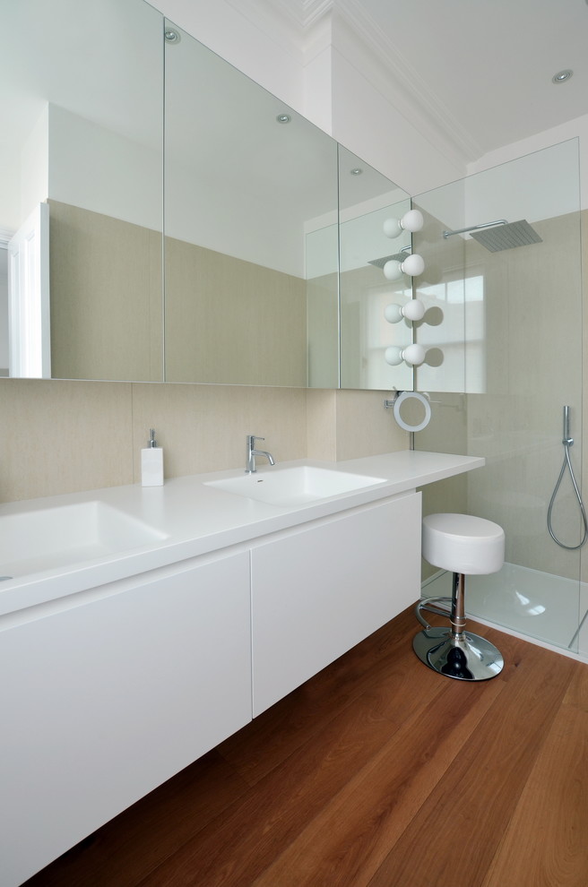 This is an example of a medium sized contemporary ensuite bathroom in London with flat-panel cabinets, white cabinets, a walk-in shower, a two-piece toilet, beige tiles, ceramic tiles, beige walls, porcelain flooring, a wall-mounted sink, solid surface worktops, brown floors, a hinged door and white worktops.
