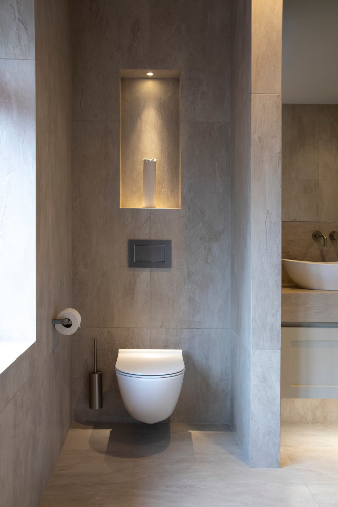 This is an example of a large contemporary ensuite bathroom in Cheshire with flat-panel cabinets, grey cabinets, a freestanding bath, a walk-in shower, a wall mounted toilet, grey tiles, ceramic tiles, grey walls, cement flooring, a trough sink, tiled worktops, grey floors, an open shower and grey worktops.