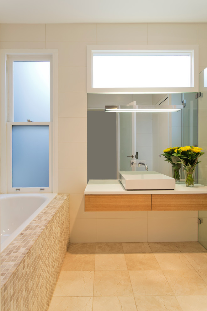 Идея дизайна: ванная комната среднего размера в современном стиле с плоскими фасадами, светлыми деревянными фасадами, ванной в нише, белой плиткой, белыми стенами, настольной раковиной и бежевым полом