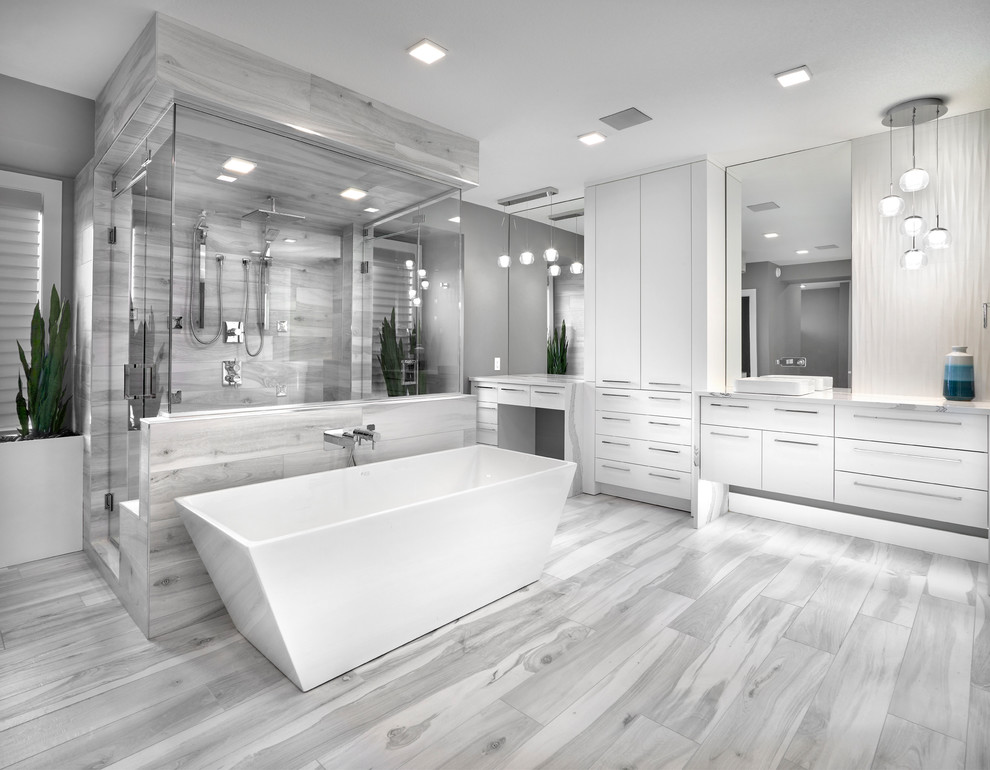 Bild på ett stort funkis grå grått en-suite badrum, med ett fristående badkar, en dubbeldusch, vit kakel, grå kakel, grå väggar, klinkergolv i keramik, ett fristående handfat, bänkskiva i kvarts, grått golv, dusch med gångjärnsdörr, porslinskakel, släta luckor och vita skåp