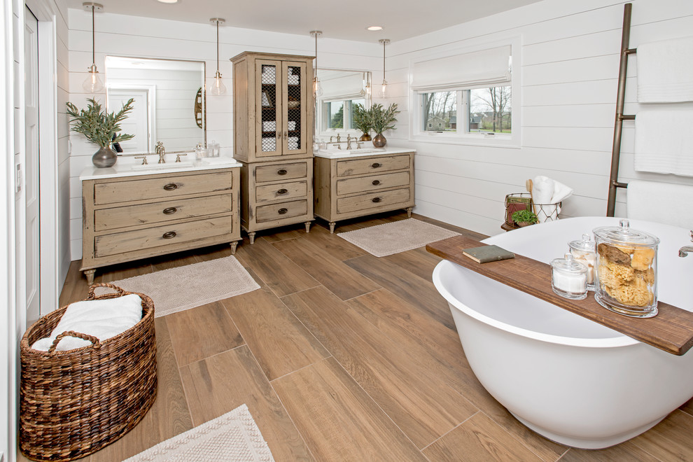 Design ideas for a large rural ensuite bathroom in Philadelphia with a freestanding bath, white tiles, white walls, brown floors, light wood cabinets, a one-piece toilet, ceramic flooring, a submerged sink, engineered stone worktops and flat-panel cabinets.