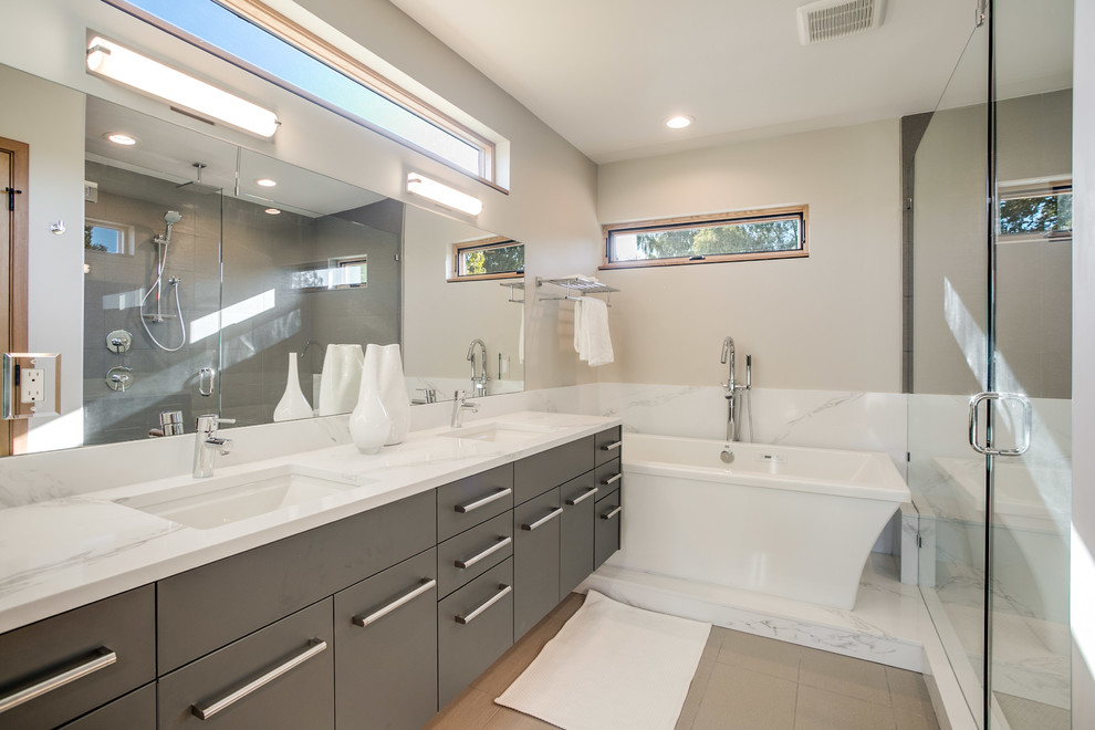Inredning av ett modernt stort en-suite badrum, med släta luckor, grå skåp, ett fristående badkar, vit kakel, stenhäll, klinkergolv i porslin, ett undermonterad handfat, bänkskiva i akrylsten, brunt golv och dusch med gångjärnsdörr