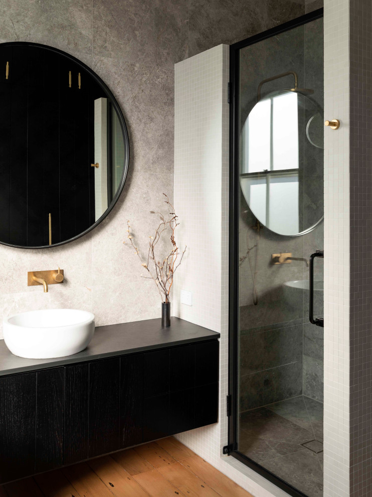 Cette image montre une douche en alcôve design avec un placard à porte plane, des portes de placard noires, un sol en bois brun, une vasque, un sol marron et un plan de toilette gris.