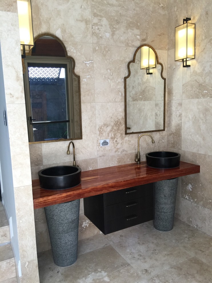 Inspiration for a tropical master beige tile and stone tile travertine floor bathroom remodel in Sunshine Coast with flat-panel cabinets, dark wood cabinets, beige walls, a pedestal sink and wood countertops