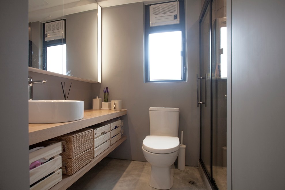 Foto di una stanza da bagno con doccia moderna di medie dimensioni con ante in legno chiaro, doccia ad angolo, WC monopezzo, pareti grigie, pavimento in cemento, lavabo a consolle, top in legno e top beige