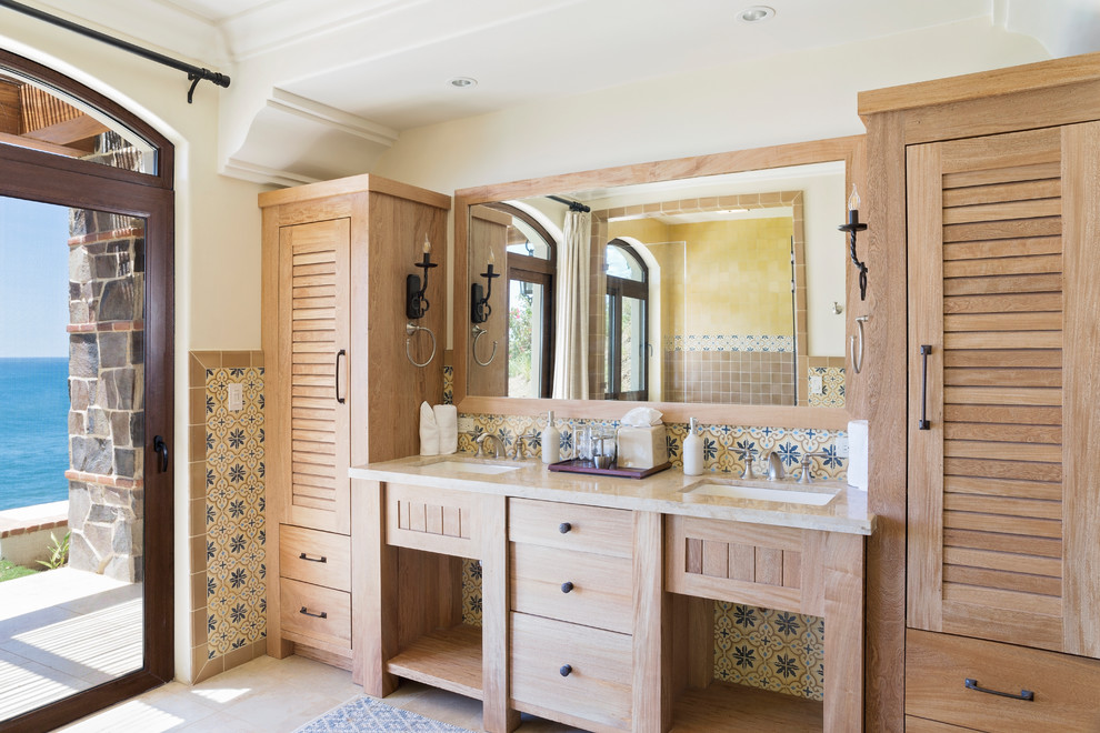 Design ideas for a mediterranean bathroom in Other with louvered cabinets, medium wood cabinets, multi-coloured tiles, white walls, a submerged sink, beige floors and beige worktops.