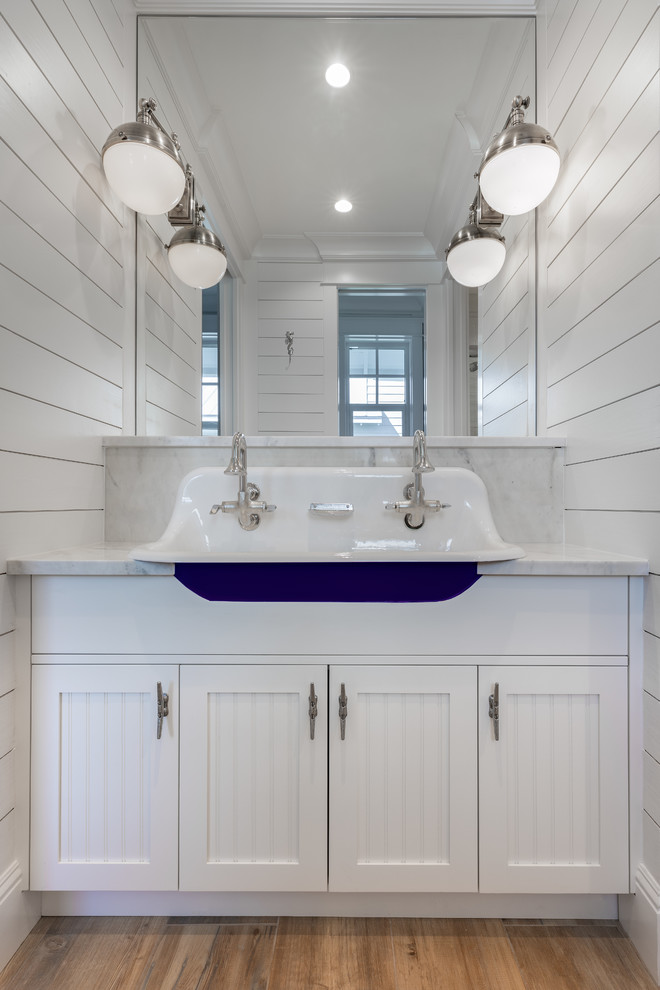 Idéer för ett litet maritimt vit badrum för barn, med luckor med infälld panel, vita skåp, vita väggar, mellanmörkt trägolv, ett undermonterad handfat och marmorbänkskiva