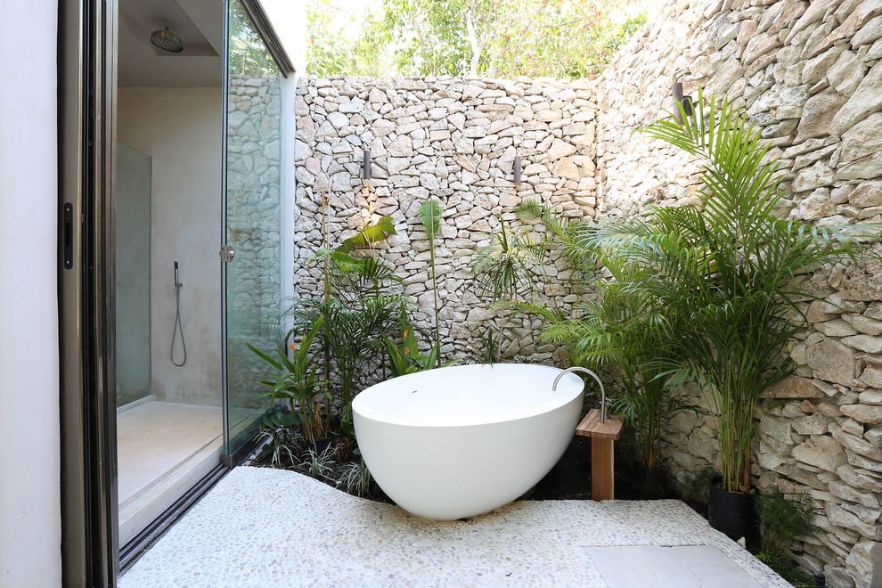 Bild på ett tropiskt en-suite badrum, med ett fristående badkar, en dusch i en alkov, beige väggar, klinkergolv i småsten, vitt golv och dusch med skjutdörr