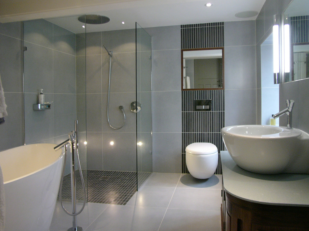 Medium sized contemporary ensuite bathroom in Other with a vessel sink, flat-panel cabinets, medium wood cabinets, solid surface worktops, a freestanding bath, a built-in shower, a wall mounted toilet, grey tiles, porcelain tiles, grey walls and porcelain flooring.