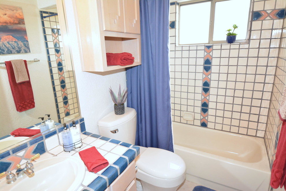 Inredning av ett amerikanskt litet badrum med dusch, med ett nedsänkt handfat, släta luckor, skåp i ljust trä, kaklad bänkskiva, ett platsbyggt badkar, en dusch/badkar-kombination, en toalettstol med separat cisternkåpa, flerfärgad kakel, keramikplattor, vita väggar och klinkergolv i terrakotta