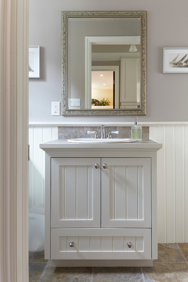 Cette photo montre une salle de bain craftsman avec un placard à porte shaker, des portes de placard blanches, un plan de toilette en carrelage, un carrelage beige et des carreaux de porcelaine.