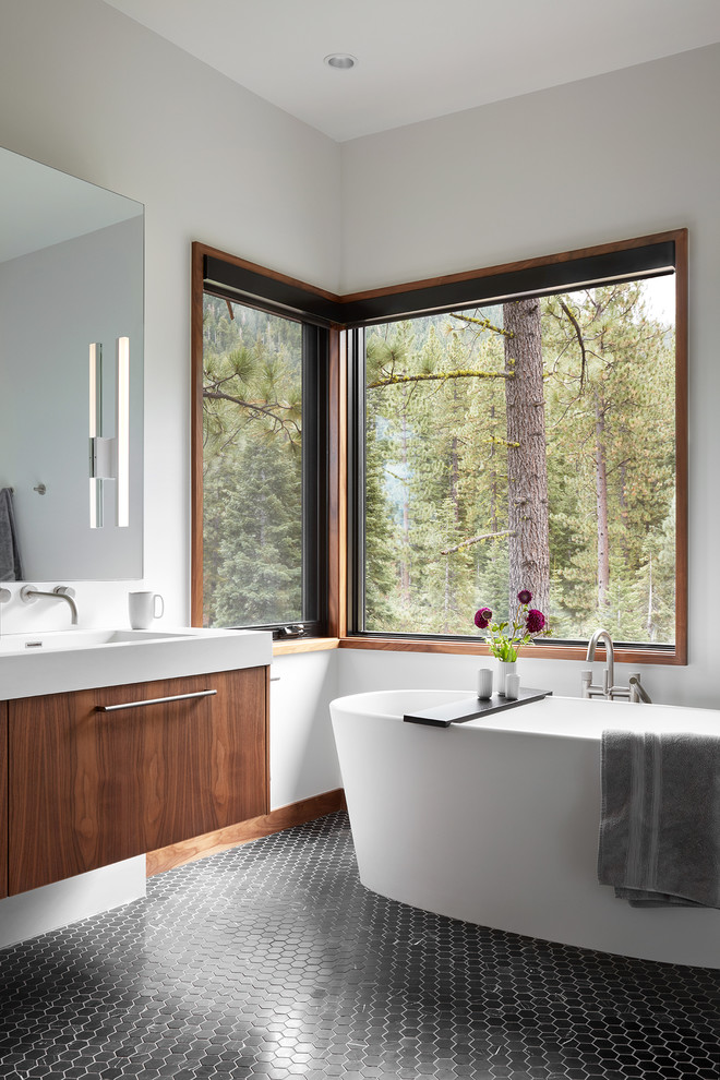 Cette photo montre une très grande salle de bain principale tendance en bois brun avec un placard à porte plane, une baignoire indépendante, un mur blanc, un sol en marbre, un lavabo intégré, un plan de toilette en quartz modifié et un sol noir.
