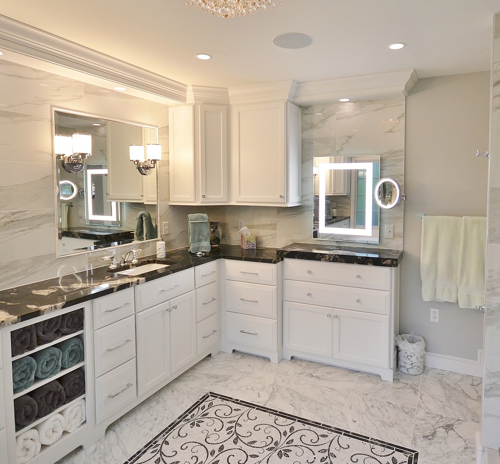 This is an example of an expansive traditional ensuite bathroom in Philadelphia with recessed-panel cabinets, white cabinets, a double shower, a one-piece toilet, white tiles, marble tiles, grey walls, vinyl flooring, a submerged sink, marble worktops, white floors, a sliding door and black worktops.