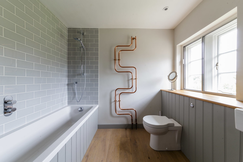 Exemple d'une salle de bain tendance de taille moyenne avec une baignoire posée, un combiné douche/baignoire, WC suspendus, un carrelage gris, des carreaux de céramique, un mur blanc, un sol en bois brun, un lavabo suspendu et un plan de toilette en bois.