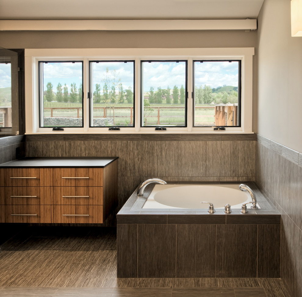 Design ideas for a large contemporary ensuite bathroom in San Francisco with flat-panel cabinets, medium wood cabinets, grey tiles, ceramic tiles, grey walls, a submerged bath, laminate floors, solid surface worktops and multi-coloured floors.