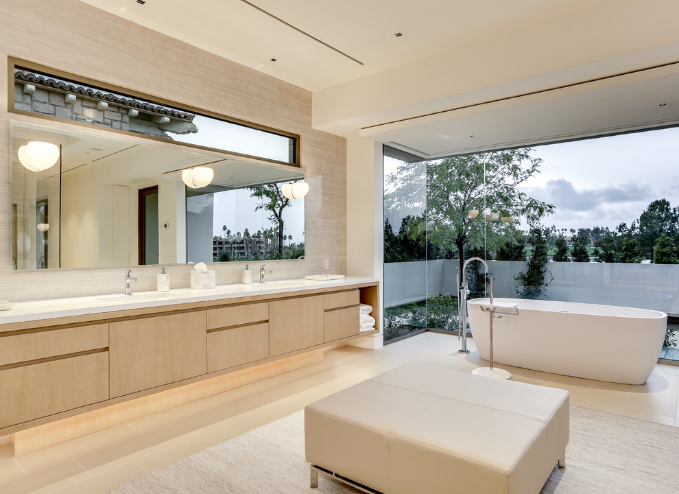 This is an example of an expansive contemporary ensuite bathroom in Los Angeles with flat-panel cabinets, light wood cabinets, a freestanding bath, beige tiles, a corner shower, beige walls, porcelain flooring, beige floors and a hinged door.