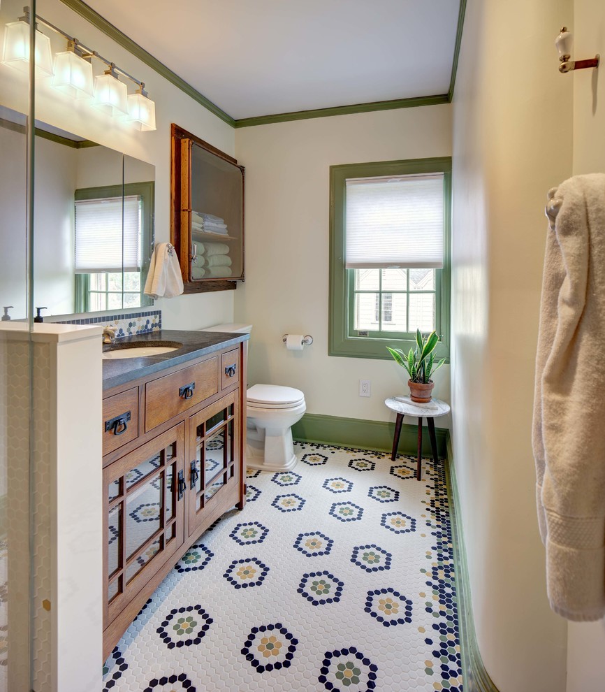 Inspiration for a mid-sized craftsman 3/4 white tile multicolored floor and mosaic tile floor corner shower remodel in New York with medium tone wood cabinets, a two-piece toilet, white walls, an undermount sink, granite countertops, a hinged shower door, gray countertops and glass-front cabinets