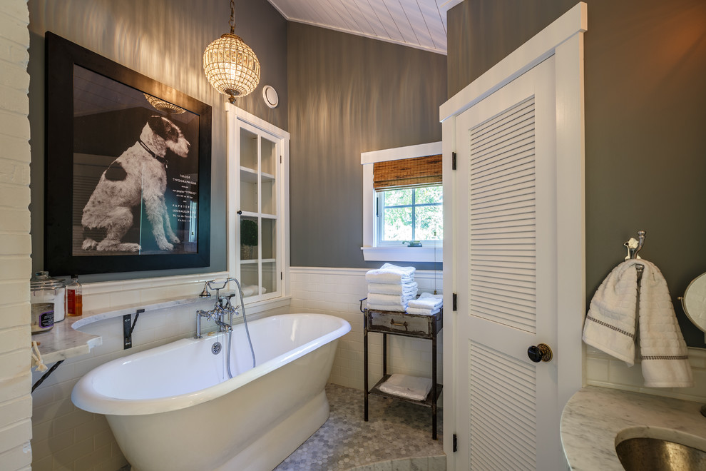 На фото: ванная комната среднего размера в морском стиле с мраморной столешницей, отдельно стоящей ванной, серой плиткой, керамогранитной плиткой, полом из галечной плитки, серыми стенами и врезной раковиной с