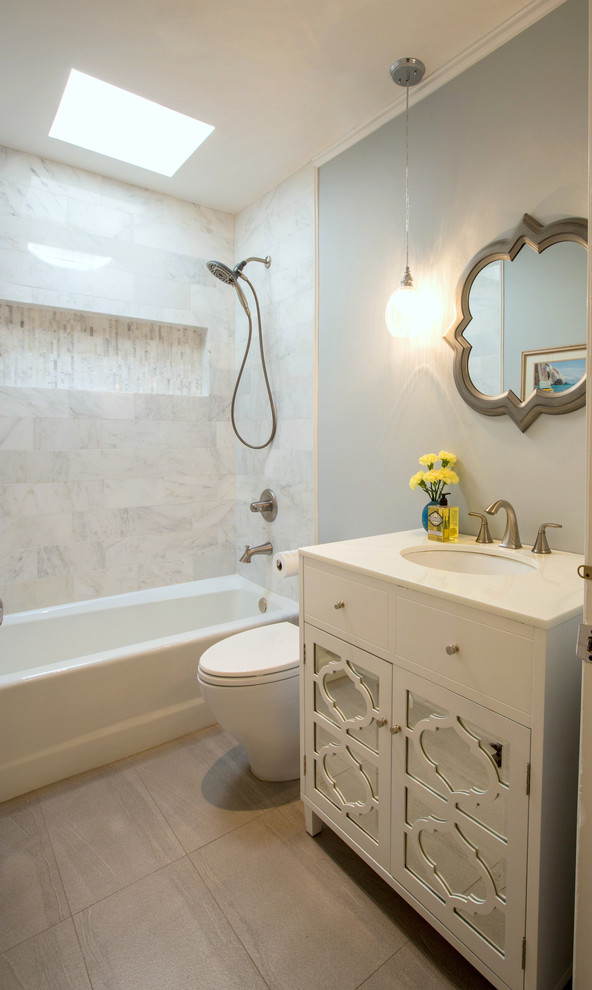 Cette image montre une salle de bain bohème de taille moyenne pour enfant avec un placard à porte vitrée, des portes de placard blanches, une baignoire en alcôve, un combiné douche/baignoire, WC à poser, un carrelage blanc, du carrelage en marbre, un mur gris, un sol en carrelage de céramique, un lavabo encastré, un plan de toilette en verre recyclé, un sol gris et une cabine de douche avec un rideau.